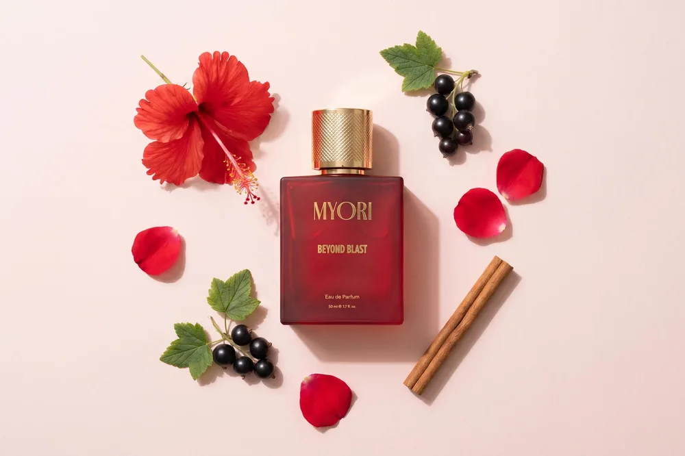 Beyond Blast şişesi, açık pembe zeminde kırmızı hibiskus çiçeği, gül yaprakları, siyah frenk üzümü ve bir tarçın çubuğu arasında